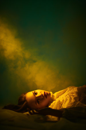 Art portrait of a beautiful tender girl with long hair, who lies on the floor in a white lace dress shrouded in haze. Beauty and Fantasy.の写真素材