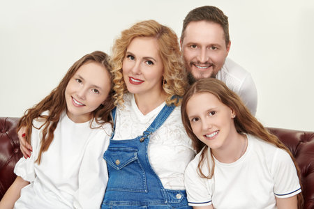 Beautiful happy mother and father with their beloved daughters posing together in white t-shirts on...