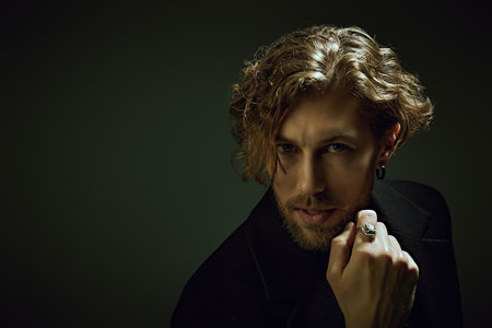 Male beauty and style. Art portrait in a dark key of a handsome forty-year-old man with curly hair, dressed in a black clothes, who looks directly into the camera. People, emotions. Copy space.の写真素材