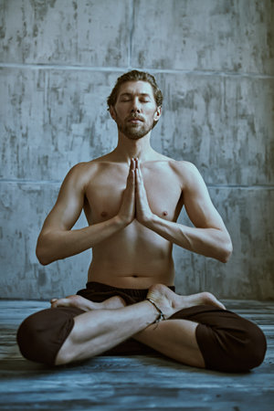 Sport and healthcare. Portrait of a handsome middle aged man sitting in lotus position on a gray studio background. Meditation. Lifestyle. Male beauty.の写真素材