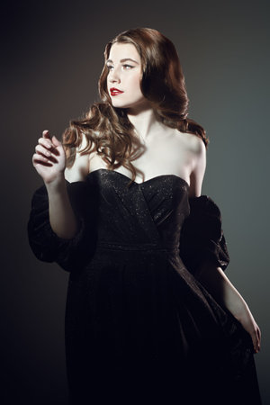 Portrait of a charming young woman in a luxury black dress on a studio background. Retro Hollywood...