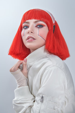 Shot of an attractive sci-fi cyborg girl with bright red makeup and stylish red hair. Cyberpunk concept. Make-up and hairstyle. White background.の写真素材