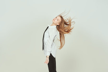 Portrait of a beautiful fashion model girl posing in dance at the studio in classic style clothes - a white blouse and a black tie. White background with copy space. Fashion shot.の写真素材