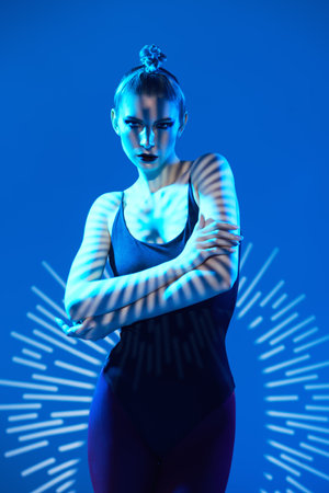 Portrait of a female model girl in a black bodysuit with dark makeup posing in shadows. Studio shot on a blue background. Make up and cosmetics.の写真素材