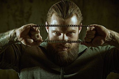 Close-up of a large brutal bearded man in a black sweatshirt with chain. The concept of masculinity...