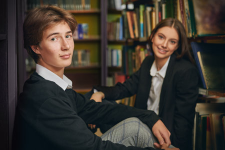 Two students wearing black and white uniform sit in a library looking with a smile at the camera. Modern generation. Education.の写真素材