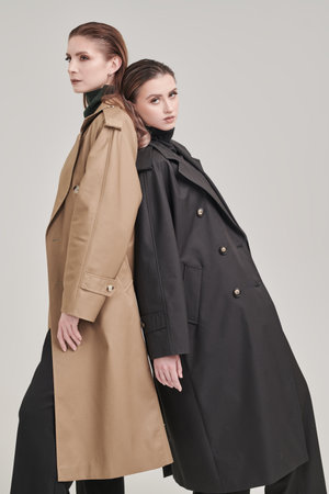 Demi-season fashion. Two confident female fashion models posing in trendy trench coats on a white studio background.の写真素材