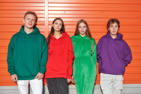 Modern youth style. Two teenage girls and two teenage boys in bright hoodies stand leaning on an...