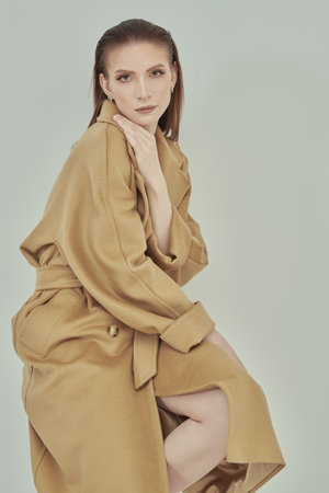 Fashion shot. Portrait of a gorgeous confident young woman posing in trendy beige felt coat. Studio portrait on a light background.の写真素材