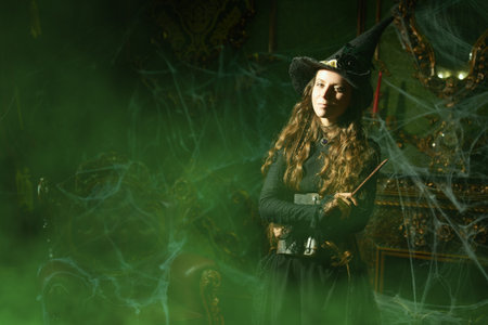 Fantasy world. Beautiful curly-haired sorceress in a black hat and dress stands in a dark old castle...