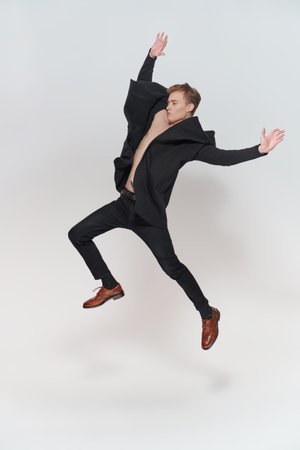A handsome cheerful young man jumping for joy and having fun. Studio full-length portrait against a...