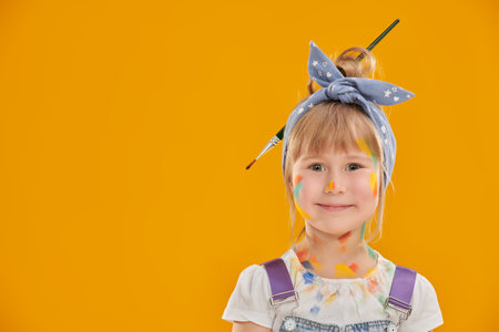 Little artist. A little cute girl, painted with colorful paints, looks happily on a yellow background with a space for text. Creativity and drawing for children. Kid's dreams and imagination.の写真素材