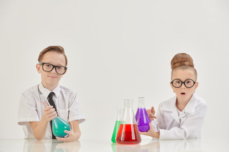 Young chemists. Two smart children, a boy and a girl, are experimenting with flasks in the laboratory. White background with copy space. Educational concept.の写真素材