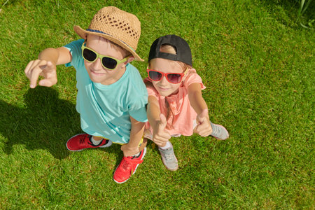 Portrait of a boy and his little sister in summer clothes and sunglasses smiling and standing in a green park on a sunny summer day. Happy summer holidays. Happy active kids.の写真素材