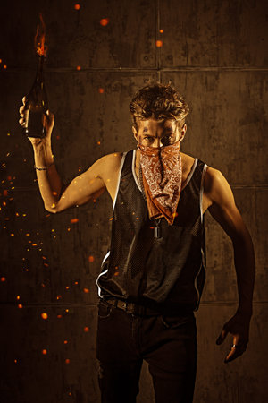 An aggressive determined man with wounds on his face and the bandana covering his face raises a...