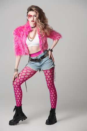 Full-length portrait of an attractive girl rock musician with bright makeup and dressed in glam rock style clothes on a white studio background. Rock star girl.の写真素材