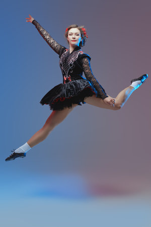 Irish dances. Professional dancer woman in national Irish costume makes a high jump during the dance. Studio full-length portrait.の写真素材