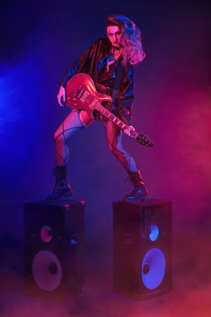 Expressive rock star girl performs with a guitar, standing on music speakers. Rock music. Glam rock style.の写真素材