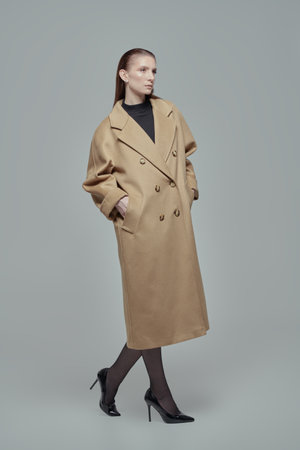 Women's fashion. Full-length shot of a stylish confident woman in a beige trench coat and high heeled leather shoes. White studio background.の写真素材