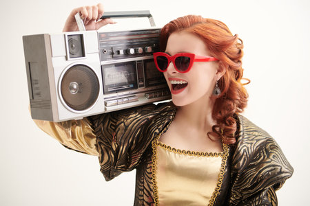 A portrait of a cool modern red-haired princess in a brown and gold dress with a stereo on a white studio background. Fairytale heroine. Tales of princesses. Disco, party.の写真素材