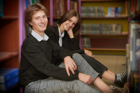 Education and modern children. Portrait of two students in uniform sitting on the floor in a library...