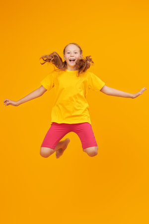 Happy children. Studio shot of a cheerful kid girl jumping with fun. Yellow background with copy...