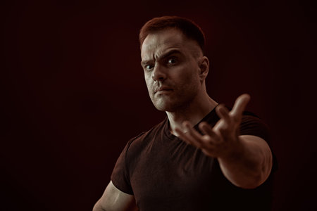 A strong muscular man expressively looks at the camera and stretches his hand forward. Studio...