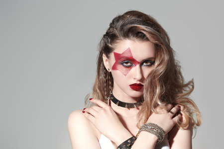 Portrait of an attractive girl rock musician with bright makeup in glam rock style on a grey studio...