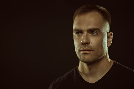 A handsome strong man confidenty looks ahead. Studio portrait on a black background with space for...