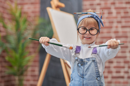 Portrait of a little cute girl in glasses who paints on an easel with brushes in her hands. Creative development of children. Happy childhood. Art studio for children.の写真素材