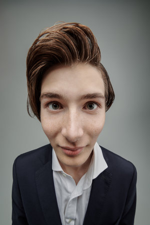 Portrait of a teenage boy in a classic suit, who stares into the camera with big eyes. Gray studio background. Modern education. People and emotions.の写真素材