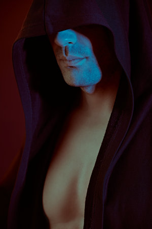 Fighter. A strong, confident man with an athletic build stands hiding his eyes under the hood. Studio portrait with mixed light. Power sports, health and active life position. Boxer.の写真素材