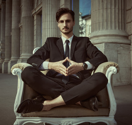 A young man in a business suit sits in an armchair on a city street. The concept of calmness and confidence.の写真素材