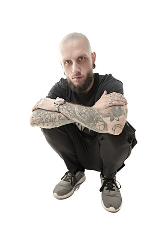 An informal brutal man with a shaved head and a beard, with tattoos on his body, dressed in black...