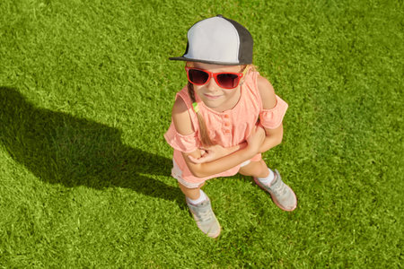 Joyful summer holidays. A happy girl in casual summer clothes and sunglasses enjoys a sunny summer day standing on the green grass.の写真素材