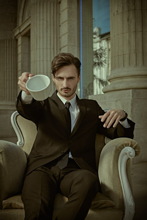 A respectable man in a classic suit sits in an armchair on the street of a big city and makes a...