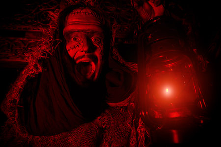 A scary medieval man with scars on his face, dressed in burlap clothes, stands with a lantern on the...