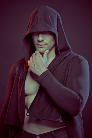 Fighter. A strong, confident man with an athletic build stands hiding his eyes under the hood. Studio portrait. Power sports, health and active life position. Boxer.の写真素材