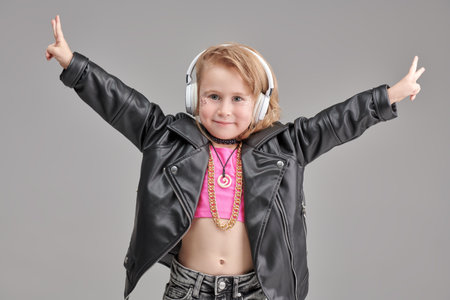 Portrait of a little cute girl with glitter makeup, in fashionable clothes and accessories of a pop and rock musician on a grey studio background. Children's fashion. Little fashion-girl.の写真素材