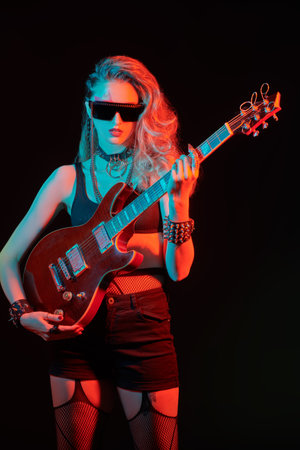 Singer, musician. Portrait of a girl rock guitarist posing with an electric guitar in sunglasses on a black background.の写真素材