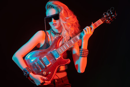 Portrait of a girl rock guitarist posing with an electric guitar in sunglasses on a black background. Singer, musician.の写真素材