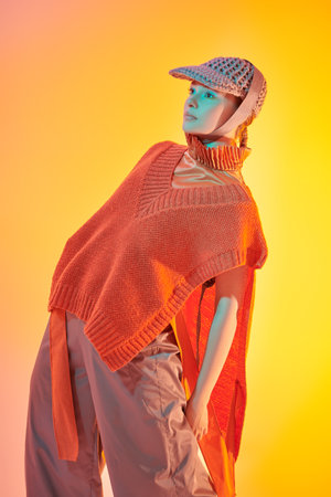 Demi-season haute couture collection. Knitwear style. Stylish fashion model posing in wide leg trousers, knitted poncho and knitted cap in studio in mixed color light. Bright colors.の写真素材