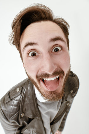 Close-up portrait of an emotional young brunette man who is looking to the camera joyfully. People and emotions. Studio white background.の写真素材