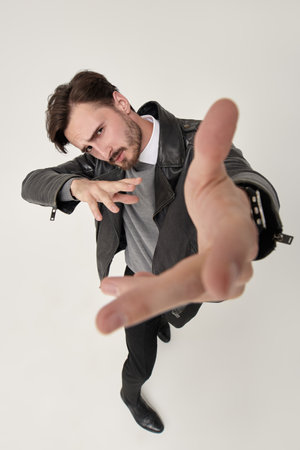 Full length portrait of handsome confident man in black trousers and black leather jacket posing in motion at studio. White background. Men's fashion.の写真素材