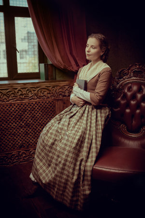 A beautiful aristocratic girl in an 18th century Scottish dress sits in a room with classic vintage...