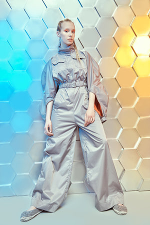 Futuristic Fashion style. Full length portrait of a beautiful female fashion model posing in a grey pantsuit on a silver technological background. High fashion.の写真素材