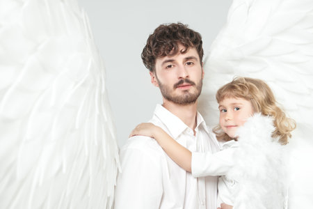 A male guardian angel holds a small baby angel in his arms. White studio background. The concept of peace, hope and goodness.の写真素材