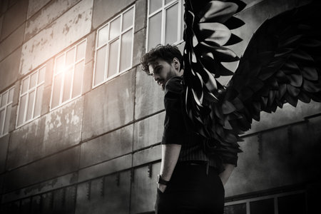 A male Black Angel stands at sunset in front of an old concrete building. Place for text. The concept of war, doomsday, Apocalypse.の写真素材