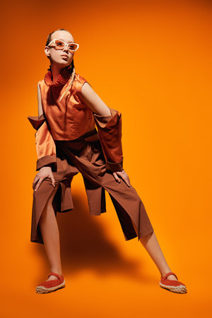 Fashion photo. Beautiful girl fashion model posing in designer clothes from the summer collection on an orange studio background. Full-length portrait.の写真素材