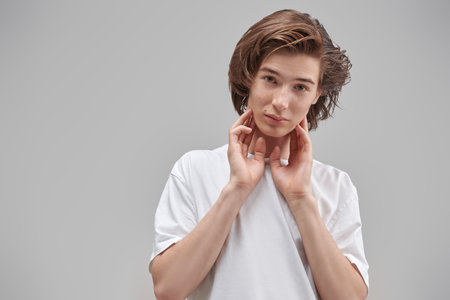 People, emotions. Portrait of handsome thoughtful teen boy in white t-shirt looking at camera. Gray background with place for text. School, education. Modern lifestyle.の写真素材